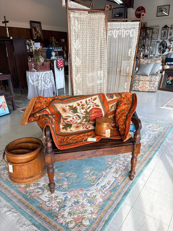 A wooden bench with a fall quilt on a rug