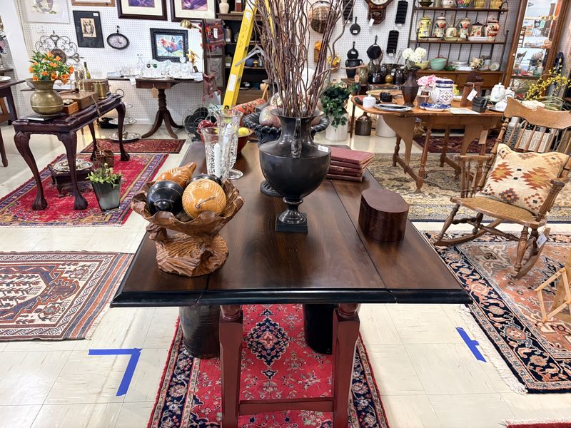 A wide view of the booth with a dark wood table, stoneware, rugs, and furniture