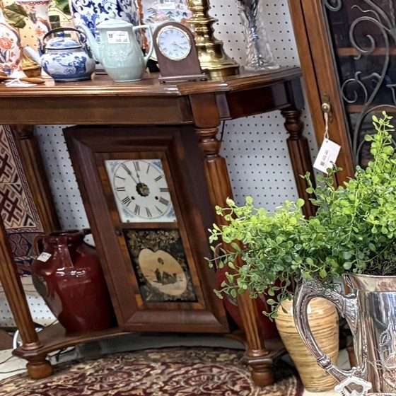 An antique shelf clock and a small mantel clock on a wooden console table