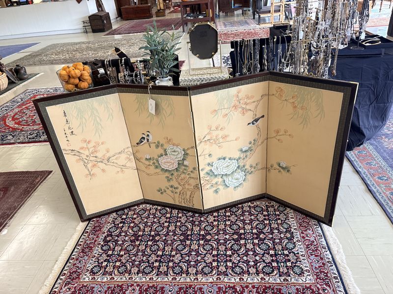 A painted Asian folding screen standing over a rug