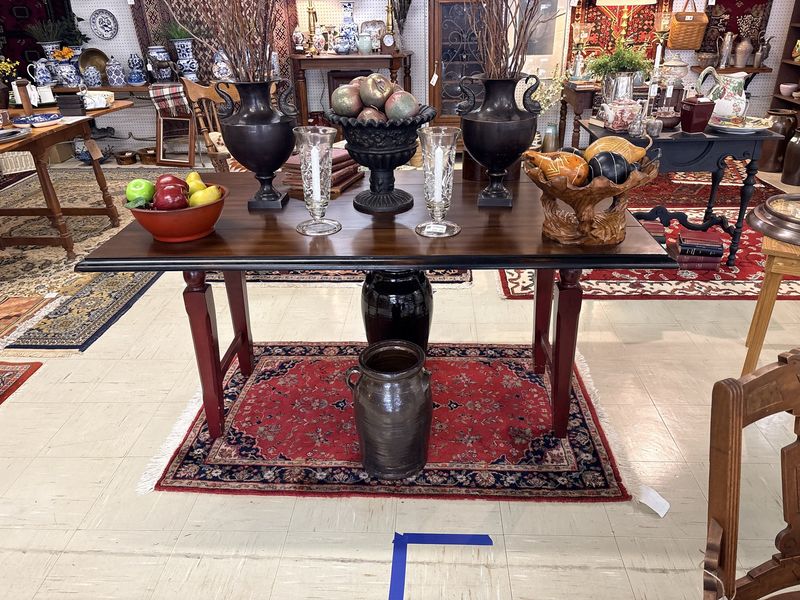 A stoneware jug beneath a dark wood table on a red Oriental rug